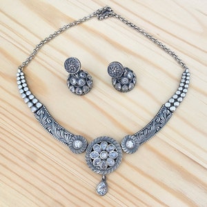 May include: A silver necklace with a floral design and a teardrop pendant. The necklace is adorned with clear stones and comes with matching earrings.