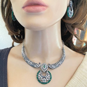 May include: Silver necklace with a green and white pendant. The pendant is a circle with a smaller circle inside. The necklace is on a mannequin.
