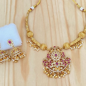 May include: A gold necklace set with a pink and white stone pendant and matching earrings. The necklace has a delicate chain with small pearl accents.