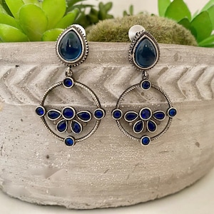 May include: Silver dangle earrings with a blue teardrop-shaped stone and a circular design with smaller blue stones.