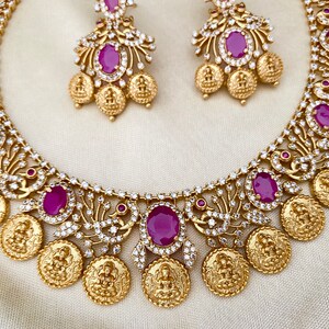 May include: A gold necklace with a coin design and pink gemstones. The necklace is paired with matching earrings.
