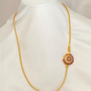May include: Gold-toned necklace with a decorative pendant. The pendant features a circular design with red and green gemstones. The necklace is displayed on a white background, showcasing the jewelry's intricate details and craftsmanship.