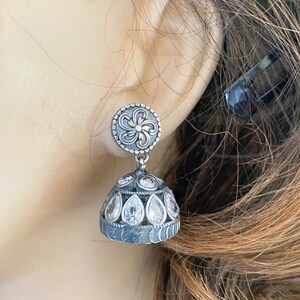 May include: Silver earrings with a floral design and clear stones. The earrings are in the shape of a teardrop and have a dangling design.