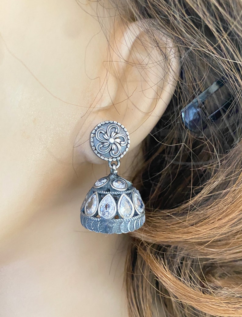 May include: Silver earrings with a floral design and clear stones. The earrings are in the shape of a teardrop and have a dangling design.