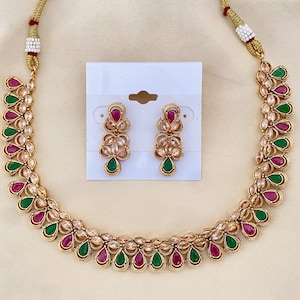 May include: A gold necklace with pink and green stones. The necklace is paired with matching earrings. The earrings are also gold with pink and green stones.