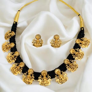 May include: A black silk thread necklace with gold-toned goddess charms and matching earrings. The necklace has a simple design and is adorned with intricate details.