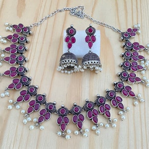 May include: A silver necklace with a pendant of pink stones and pearl accents. Matching earrings with pink stones and pearl accents.