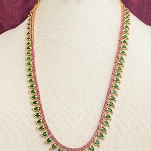 May include: A gold necklace with pink and green stones. The necklace is made of small, teardrop-shaped stones that are strung together in a long, flowing design. The necklace is accented with small, round stones that are set in the center of each teardrop-shaped stone.