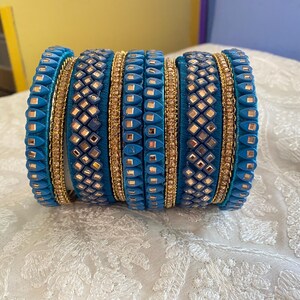 May include: A stack of blue bangles with gold accents. The bangles have a textured design with small, square-shaped embellishments and gold bands. The bangles are stacked together, showcasing their intricate details and vibrant colors.