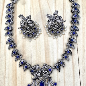 May include: A silver necklace with a peacock design and blue stones. The necklace has a matching pair of earrings with a peacock design and blue stones.
