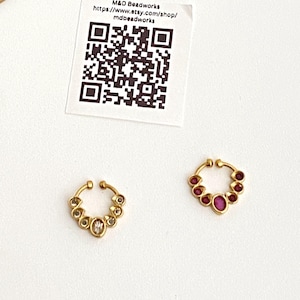 May include: Two gold-toned septum rings featuring a circular design with small stones. One ring has clear white stones, and the other has deep pink stones. A square paper card with a QR code and the text M&D Beadworks https://www.etsy.com/shop/mdbeadworks is included.