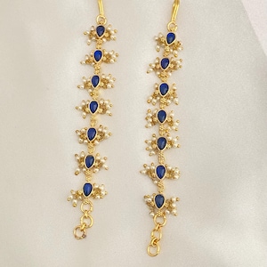 May include: Two gold-colored hair accessories with a series of blue teardrop-shaped gemstones and small white pearls. The accessories have a delicate chain at the bottom and a hook at the top.
