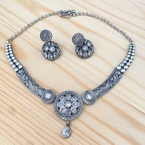 May include: A silver necklace with a floral design and clear stones. The necklace is paired with matching earrings.