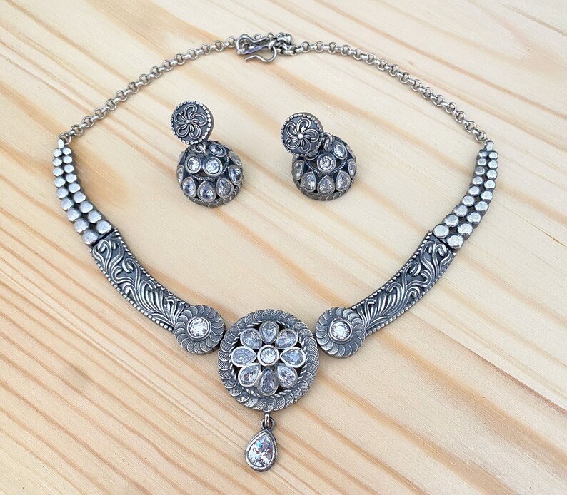 May include: A silver necklace with a floral design and clear stones. The necklace is paired with matching earrings.