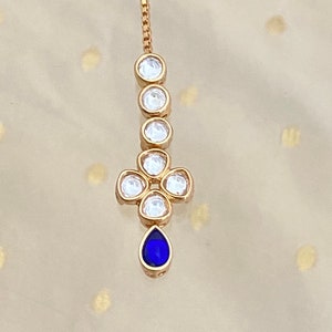 May include: A gold chain with a teardrop-shaped blue gemstone pendant. The pendant is surrounded by a cluster of clear round gemstones.