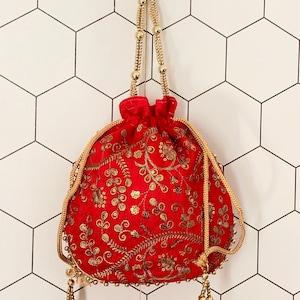 May include: A red velvet drawstring bag with gold embroidery and beaded trim. The bag has a gold chain handle and tassel accents.