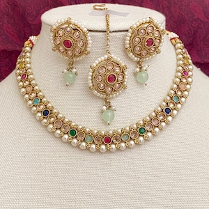 May include: A gold necklace with a double strand of white pearls and colorful stones. The necklace comes with matching earrings and a pendant with a red stone in the center.