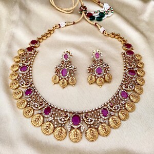 May include: A gold necklace with a coin design and pink gemstones. The necklace is paired with matching earrings.