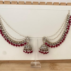 May include: A pair of gold-tone jhumka earrings featuring intricate metalwork, inset mirrors, and dangling fuchsia beads. Each earring is connected to a multi-layered chain strand adorned with small white pearls and fuchsia beads.