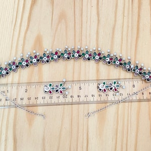 Op de afbeelding: Een zilveren choker ketting met een bloemenontwerp. De ketting is versierd met kleurrijke emaille bloemen en witte parel accenten. De ketting is 48 cm lang en heeft een verstelbare ketting.
