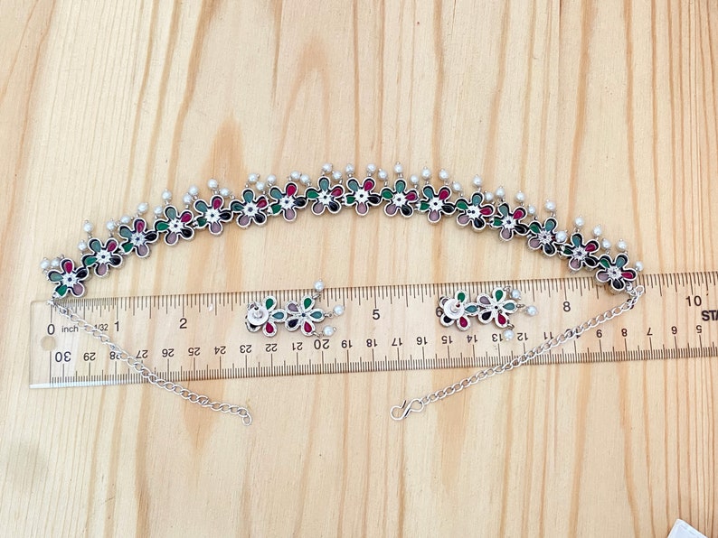Op de afbeelding: Een zilveren choker ketting met een bloemenontwerp. De ketting is versierd met kleurrijke emaille bloemen en witte parel accenten. De ketting is 48 cm lang en heeft een verstelbare ketting.