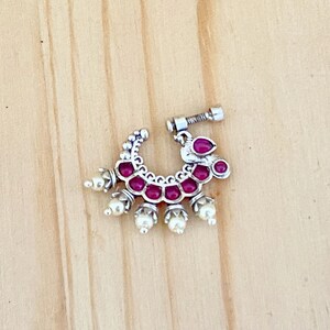 May include: Silver nose ring with a pink stone design and white pearl accents.