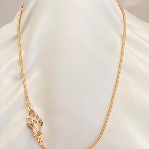May include: Gold-toned necklace with a decorative pendant. The pendant features a floral design with red, green, and white gemstones. The chain has a delicate, woven pattern. The necklace is displayed against a white background.