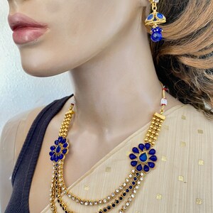 Puede incluir: Un collar de oro con tres hileras de piedras azules y transparentes. El collar tiene un dise&ntilde;o de flor con una piedra azul en el centro. El collar se combina con pendientes a juego con una piedra azul y un colgante.