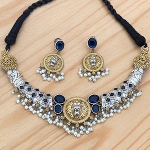 May include: A silver and gold necklace with a lion head pendant and blue and white accents. The necklace is paired with matching earrings.
