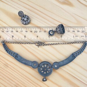 May include: A silver necklace with a large circular pendant featuring a floral design and small stones. The necklace is 18 inches long and comes with a pair of matching earrings.