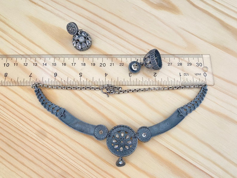 May include: A silver necklace with a large circular pendant featuring a floral design and small stones. The necklace is 18 inches long and comes with a pair of matching earrings.