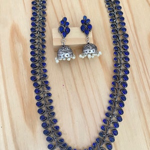 May include: A silver necklace and earrings set with blue stones. The necklace is a long chain with a design of leaves and blue stones. The earrings are dangle earrings with a similar design.