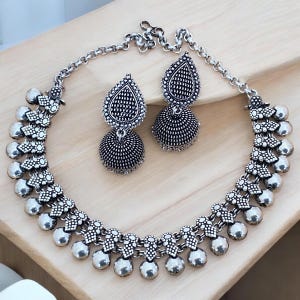May include: A silver necklace with a teardrop-shaped pendant and a matching pair of earrings. The necklace has a chain with small round beads and a decorative design. The earrings are also teardrop-shaped with a round bead at the top.