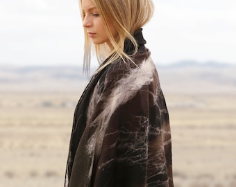 May include: A woman wearing a black and brown patterned scarf with a white background. The scarf is draped over her shoulders and is made of a soft, flowing fabric.
