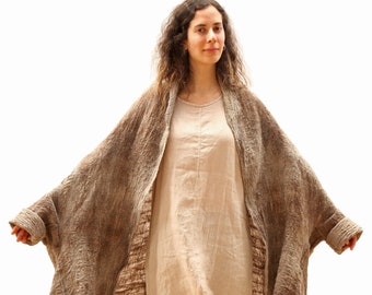 May include: A long, brown and grey, textured, linen cardigan with a loose fit. The cardigan is worn over a light beige, linen dress and blue jeans.