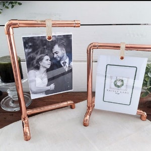 May include: Two copper pipe picture frames with a rustic look. The larger frame holds a black and white photo of a couple. The smaller frame holds a white card with the text "Rainny Lane Designs".