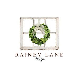 May include: A white window frame with a green boxwood wreath hanging from a white ribbon. The text "Rainey Lane design" is below the window frame.