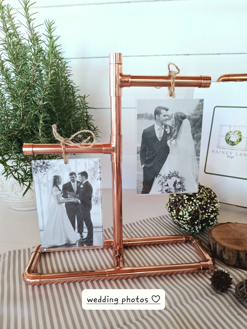May include: Copper pipe photo display stand with two black and white wedding photos and a card with the text "Rainey Lane Design".