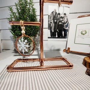 May include: Copper pipe stand with three tiers for displaying ornaments and a photo. The stand has a rustic look and is perfect for adding a touch of farmhouse style to your home decor.