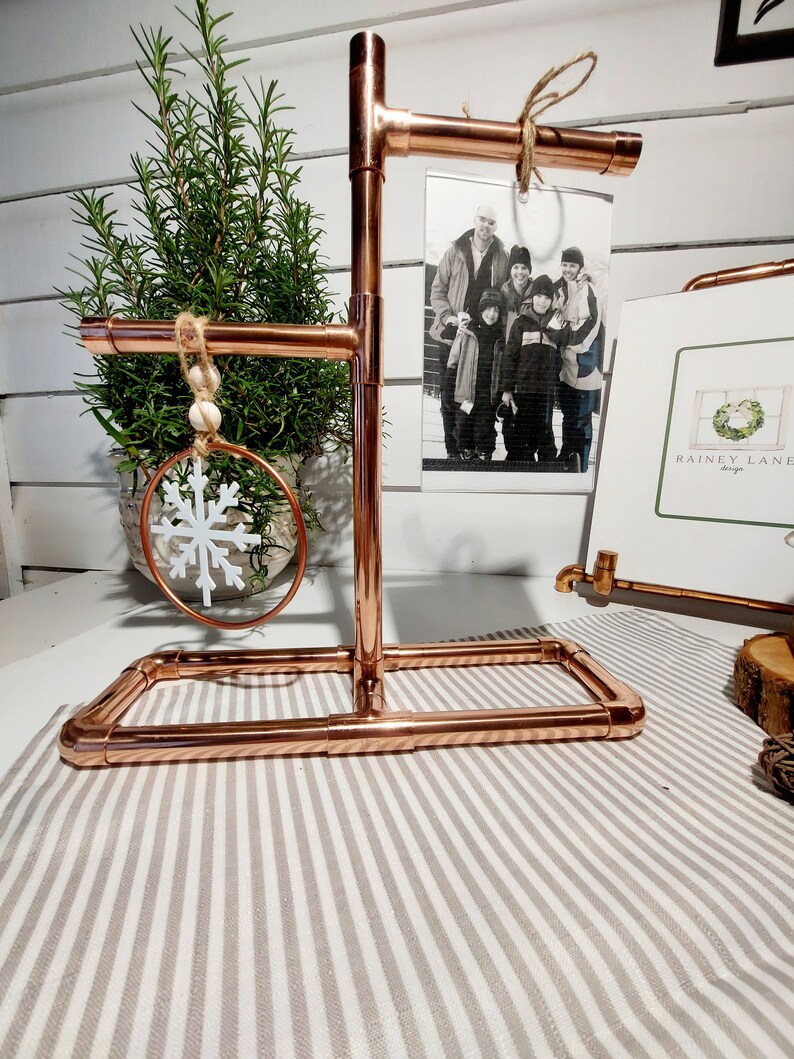 May include: Copper pipe stand with three tiers for displaying ornaments and a photo. The stand has a rustic look and is perfect for adding a touch of farmhouse style to your home decor.