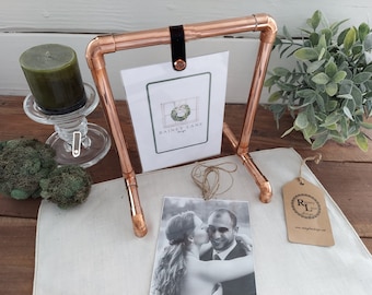 May include: Copper pipe picture frame with a black leather strap and a white card with the text "Rainy Lane Designs". The frame is holding a black and white photo of a couple.
