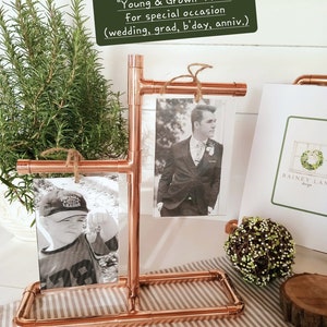May include: Copper pipe picture frame stand with two black and white photos. The stand is on a white and brown striped surface. The text on the sign reads "Young & Grown" Pics for special occasion (wedding, grad, b'day, anniv.)
