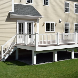 May include: A raised outdoor deck with dark brown composite flooring and white railings, featuring a staircase leading to a set of white French doors on a house with beige horizontal siding and multiple rectangular windows.