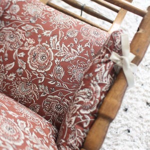 Pode incluir: Uma cadeira de madeira com um almofada de padr&atilde;o floral vermelho e branco. A cadeira &eacute; feita de madeira e tem um design simples.