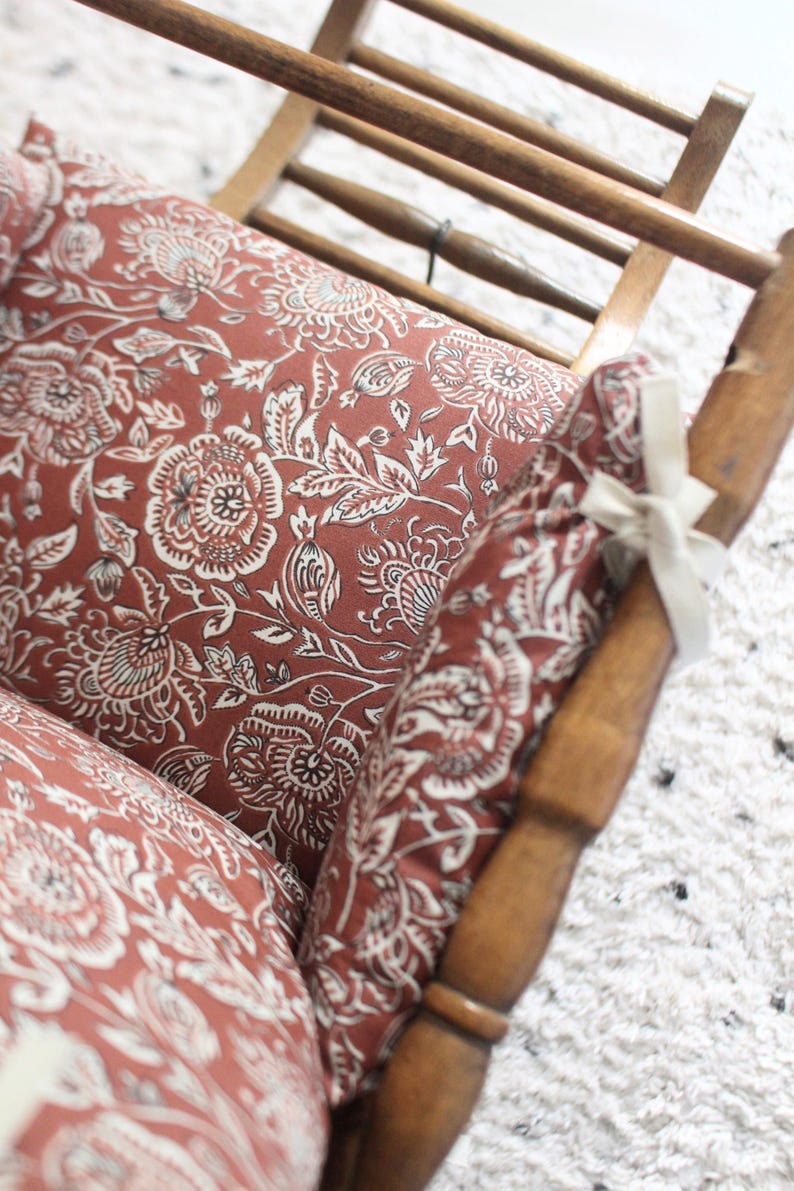 Pode incluir: Uma cadeira de madeira com um almofada de padr&atilde;o floral vermelho e branco. A cadeira &eacute; feita de madeira e tem um design simples.