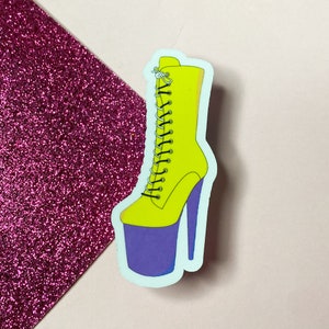 Puede incluir: Una bota amarilla con una plataforma morada y cordones negros. La bota tiene un tacón alto y es una pegatina.