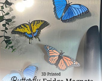 May include: 3D printed butterfly fridge magnets in various colors, including blue, orange, yellow, and red. The magnets are designed to resemble different butterfly species and are attached to a metallic surface.