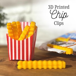 May include: A set of 3D-printed chip clips in the shape of french fries. The clips are yellow and have a crinkle-cut design. They are displayed in a red and white striped container, with the text "3D Printed Chip Clips".