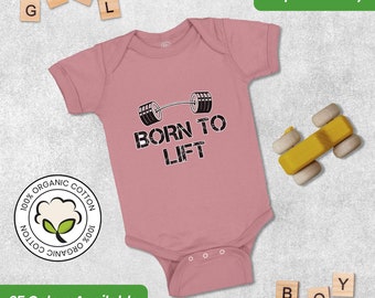 May include: A pink baby onesie with short sleeves and a white cotton graphic that says "Born to Lift" with a barbell design. The onesie is made of 100% organic cotton.