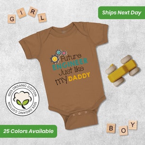 May include: A brown baby onesie with a graphic of gears and the text "Future Engineer Just like my Daddy". The onesie is made of 100% organic cotton.